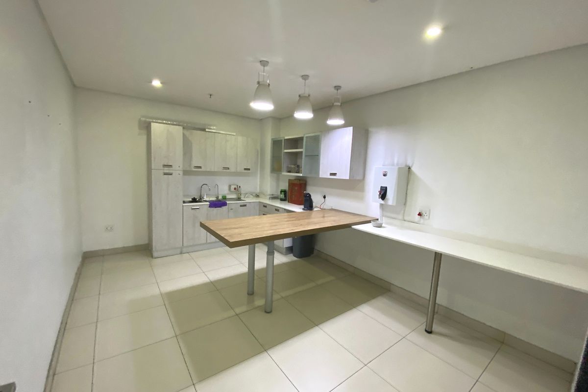 A clean, functional industrial kitchen area featuring built-in cabinetry, a stainless steel sink, tiled flooring, and a fixed breakfast bar with pendant lighting.