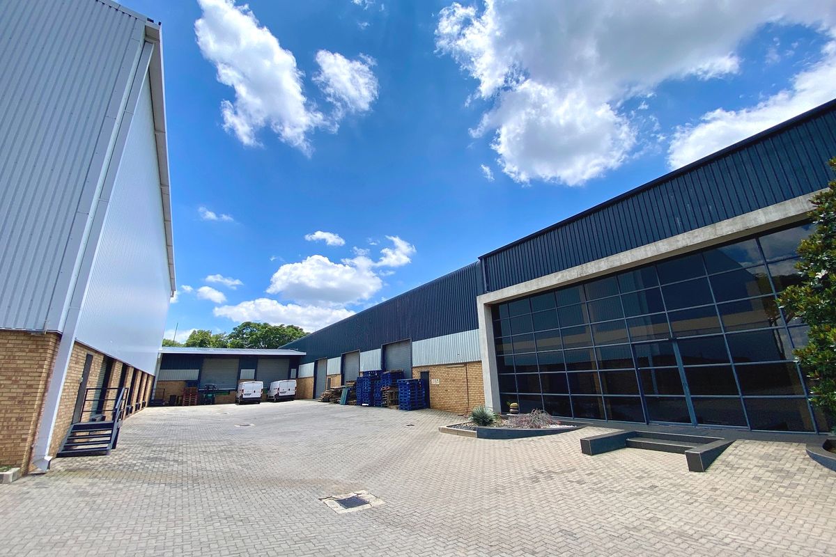 Spacious industrial yard featuring paved surfacing, large glass facade, metal cladding, and multiple roller shutter access points for efficient logistics and operations.