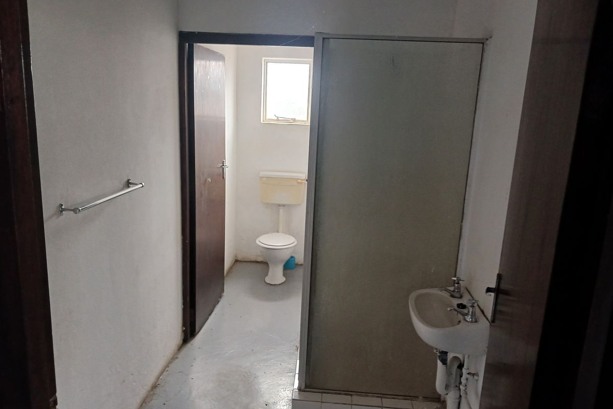 A functional bathroom featuring a shower cubicle, wall-mounted basin, and separate toilet area, requiring cosmetic updates to improve its overall condition.