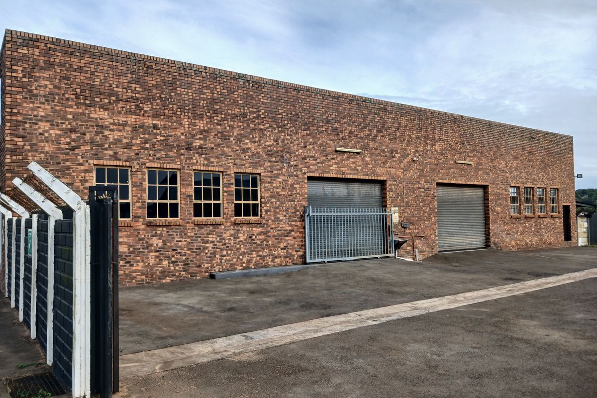 Commercial industrial building featuring a face brick facade, multiple roller shutter doors, and secure gated access with an asphalt driveway.