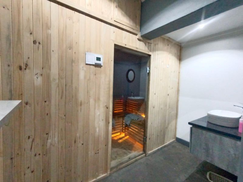 A dedicated sauna room featuring timber wall cladding, a glass door, and an adjacent vanity area with a stone countertop.