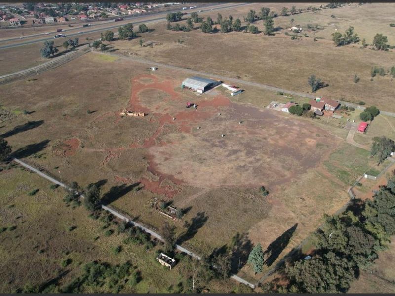 Aerial view of a large industrial plot featuring an existing shed, outbuildings, and extensive undeveloped land with highway access.