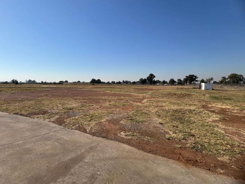 Expansive vacant industrial land featuring a concrete driveway and perimeter fencing, offering significant development potential.