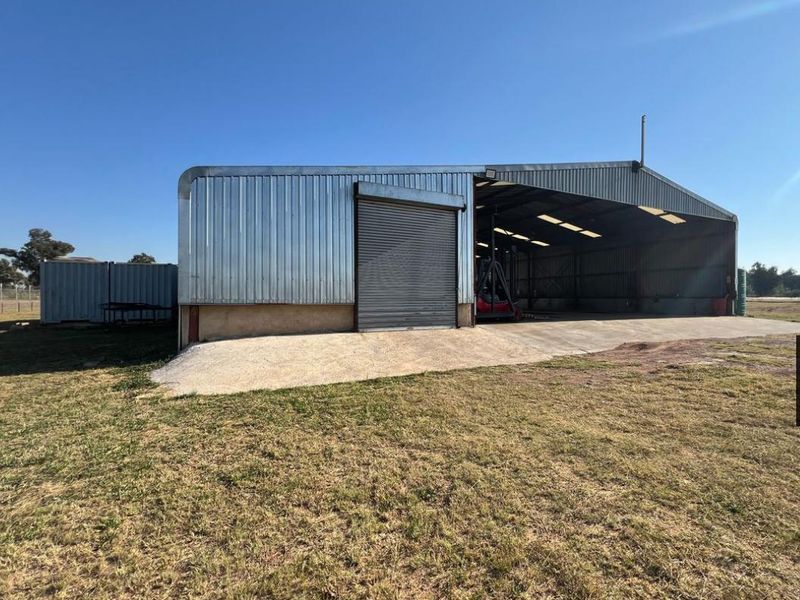 Industrial warehouse featuring corrugated metal cladding, a large roller shutter door, and a concrete apron, set on a spacious open site.