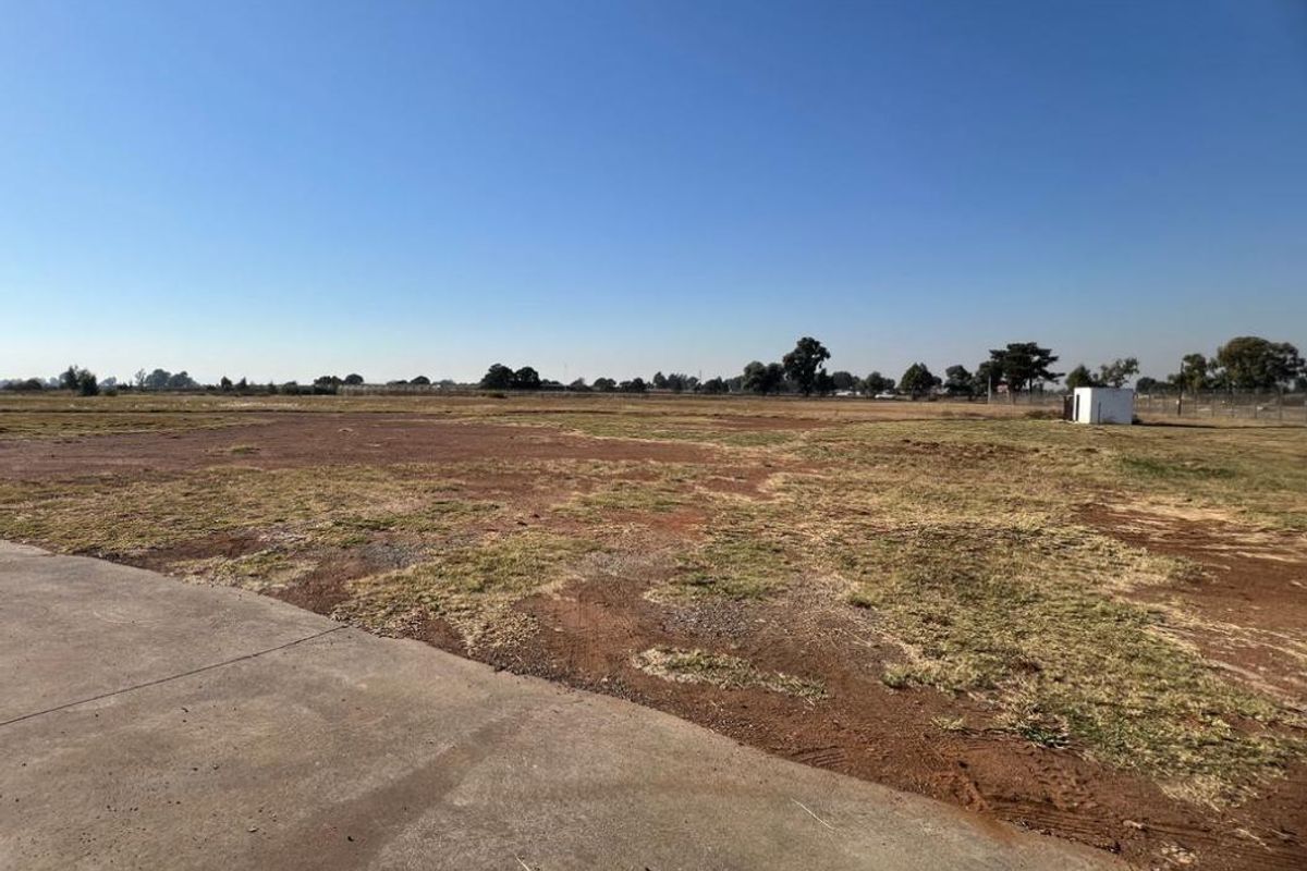 Expansive vacant industrial land featuring a concrete driveway and perimeter fencing, offering significant development potential.
