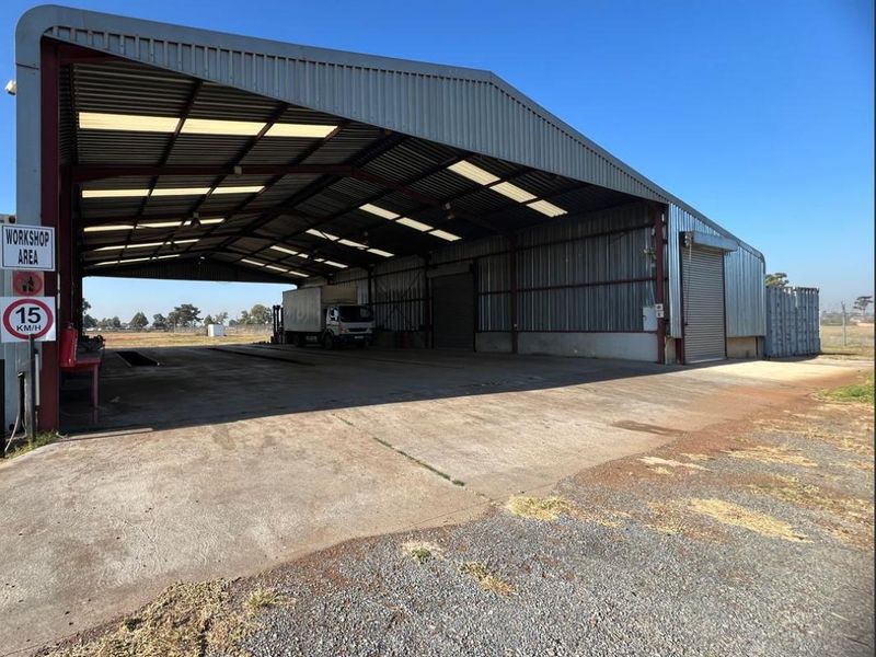 Large industrial workshop area featuring a steel portal frame structure, corrugated metal cladding, and expansive concrete hardstand suitable for heavy vehicle access.
