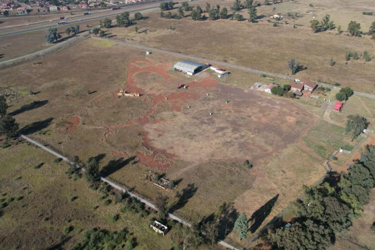 Aerial view of a large industrial plot featuring an existing shed, outbuildings, and extensive undeveloped land with highway access.