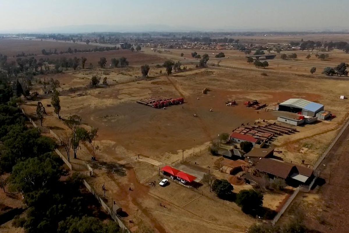 Aerial view of an industrial property featuring a large yard, warehouse structure, and perimeter fencing, situated in an open landscape.