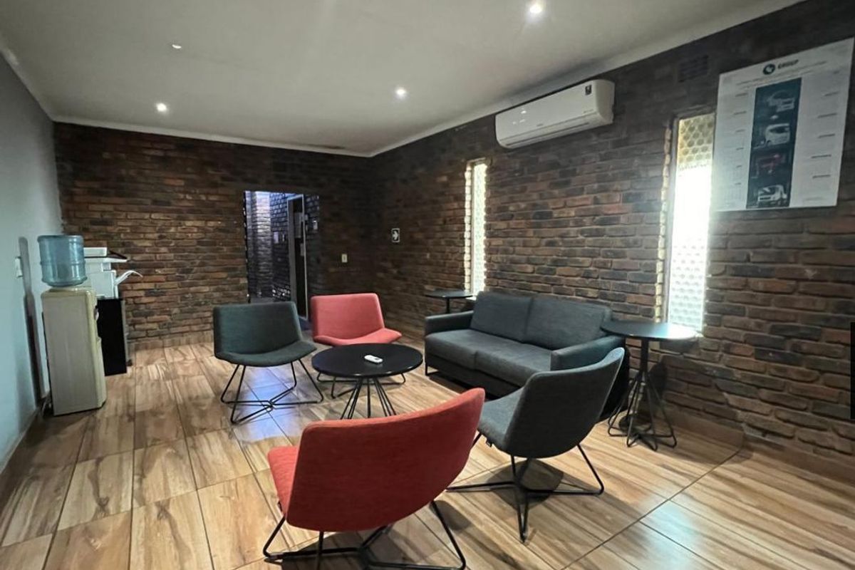 A modern industrial-style lounge area featuring exposed brick walls, wood-look tile flooring, and a wall-mounted air conditioning unit.
