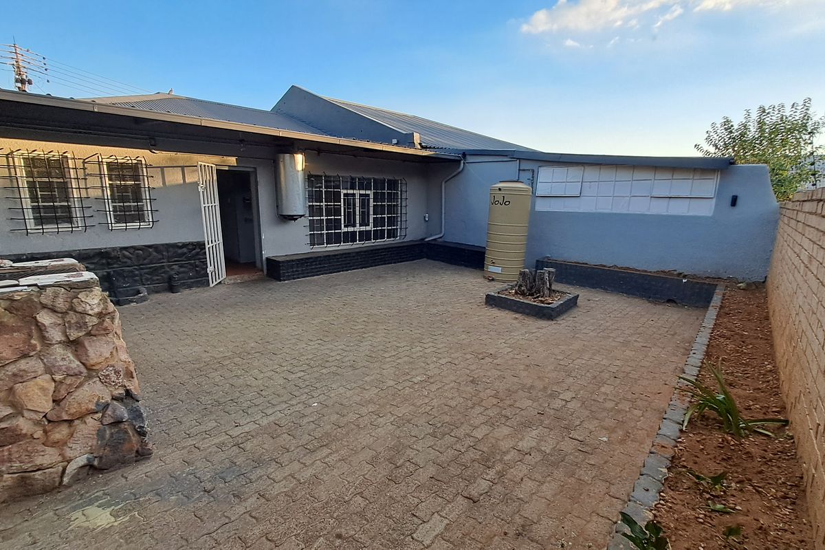Rear exterior courtyard featuring paved flooring, a water storage tank, stone feature wall, and secure boundary wall with electric fencing.