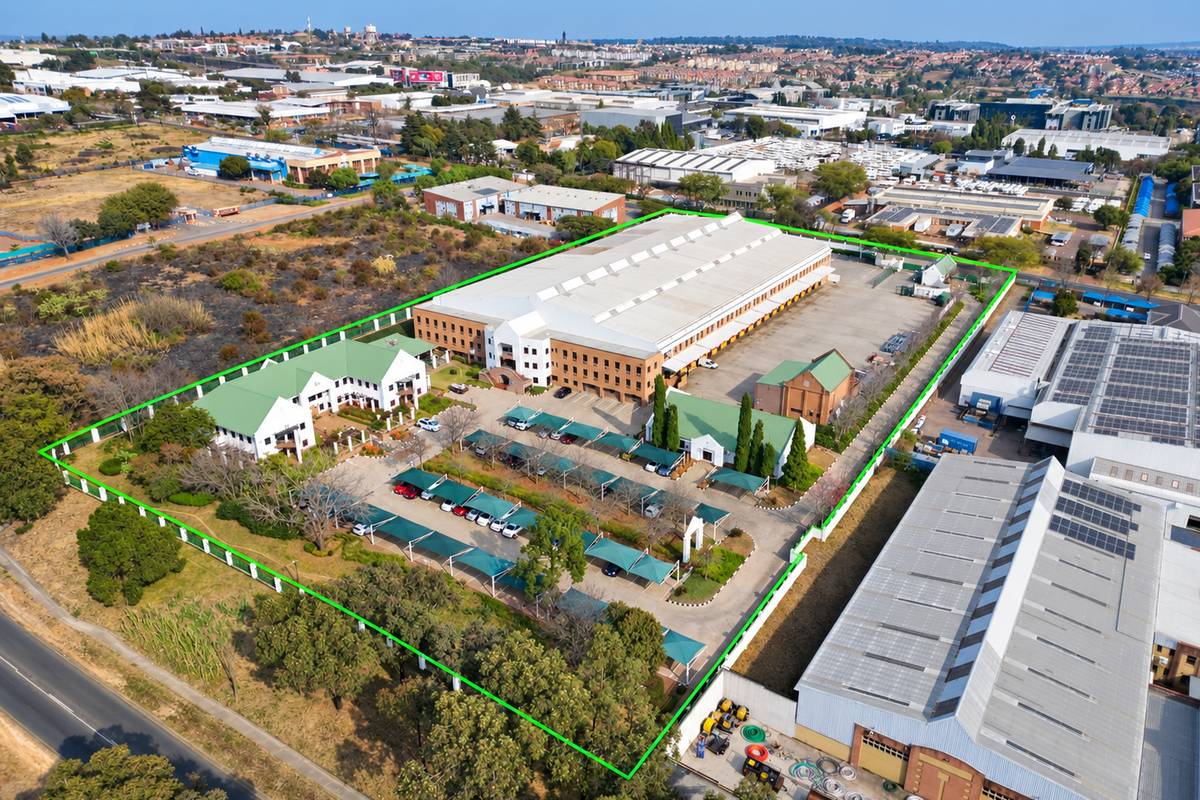 Aerial view of a large industrial property featuring a warehouse, office complex, and extensive paved parking with shade cloth carports within a fenced perimeter.