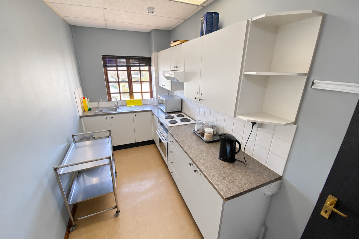 Compact industrial kitchen featuring built-in cabinetry, laminate countertops, electric hob, oven, and stainless steel sink with tiled splashback.