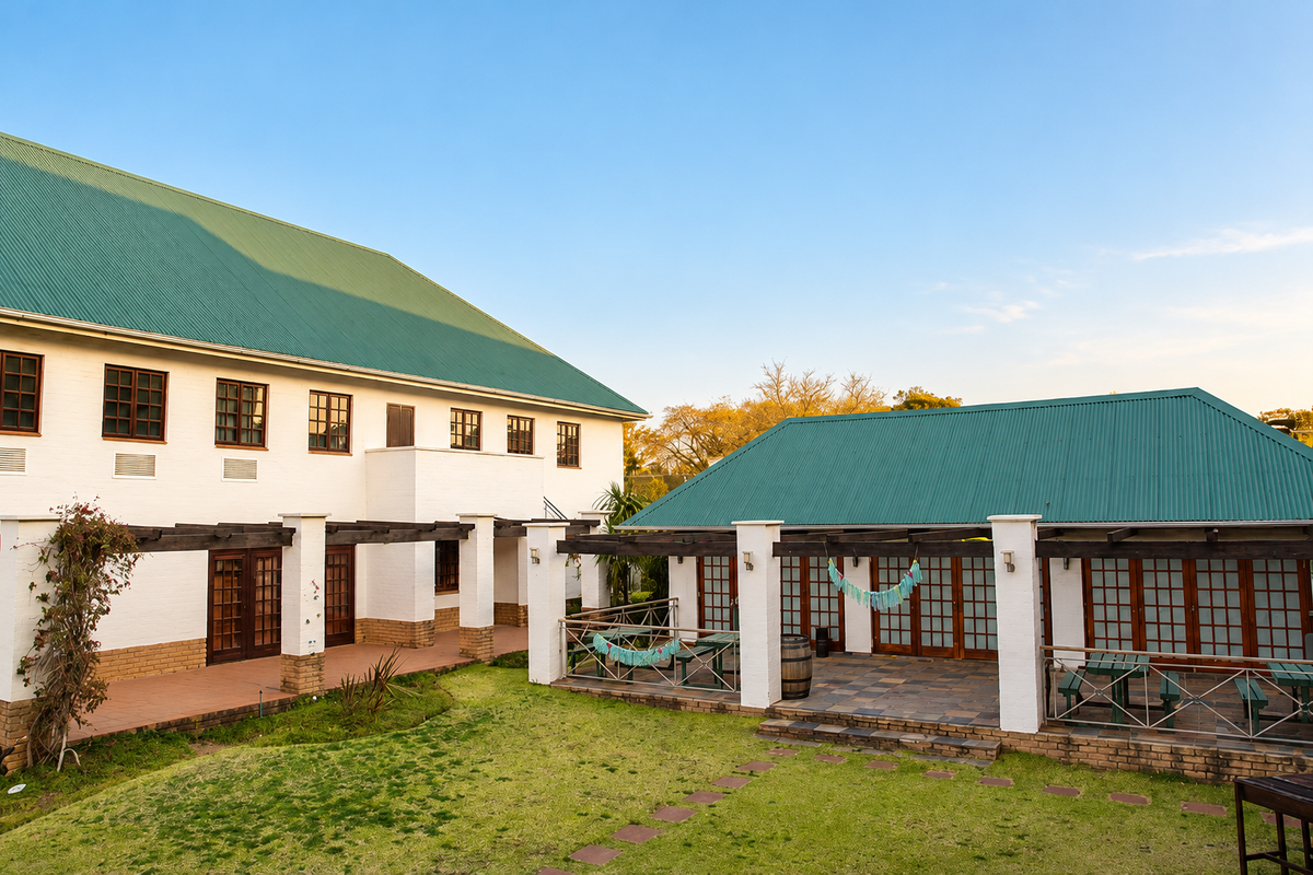 Rear view of the industrial property featuring a large lawn, paved patio areas, timber pergolas, and distinctive green corrugated metal roofing.