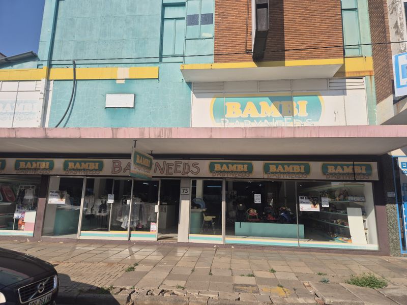 Front elevation of a retail storefront featuring large display windows, a concrete awning, and prominent signage on a multi-textured brick and painted facade.