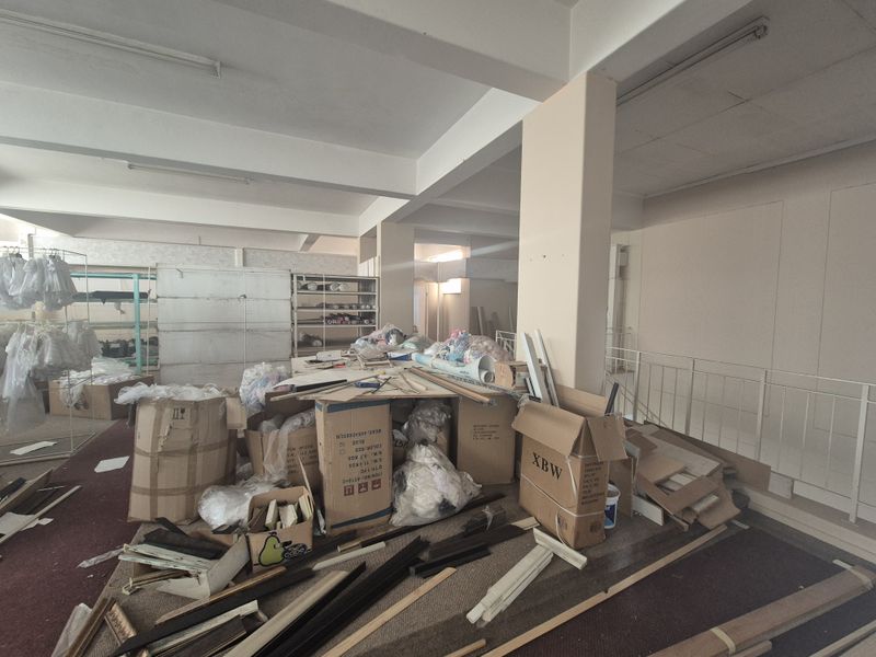 Spacious open-plan retail area featuring structural support columns, overhead fluorescent lighting, and built-in shelving units, currently requiring clearing and refurbishment.