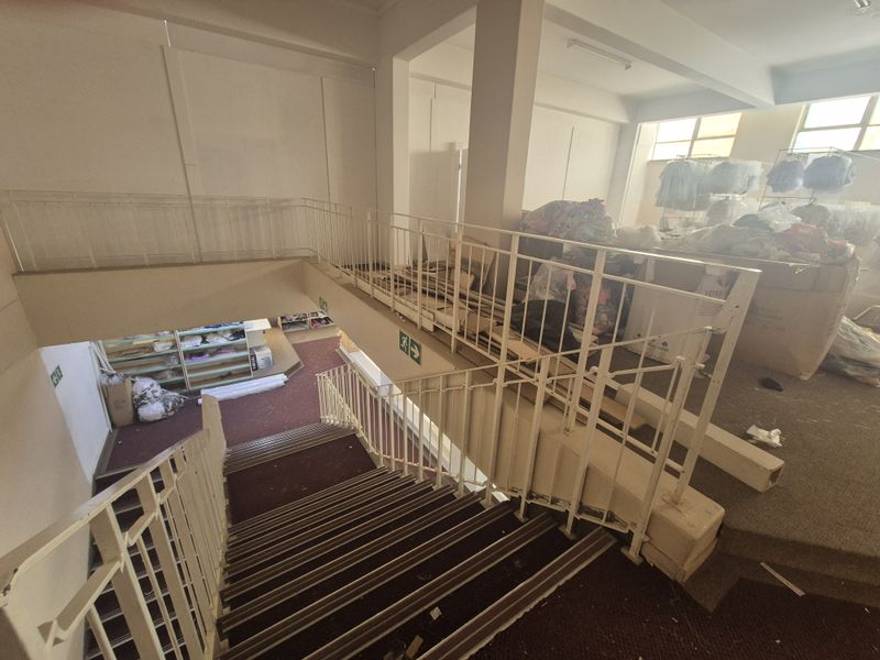 Interior staircase area connecting levels in a retail space, featuring metal balustrades and carpeted steps, currently used for storage.
