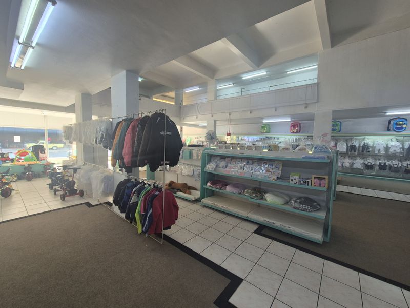 Spacious open-plan retail area featuring tiled and carpeted flooring, structural columns, and a mezzanine level with integrated fluorescent lighting.