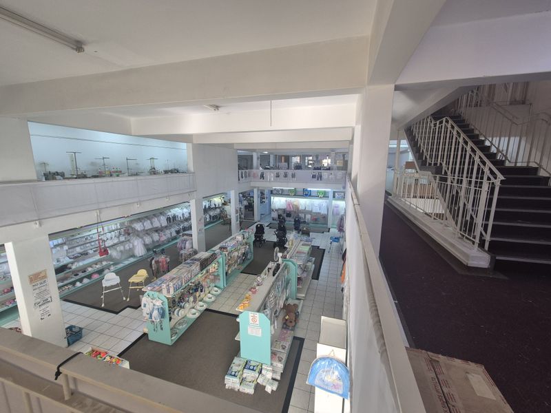 Spacious retail interior featuring a mezzanine level, open-plan layout, tiled flooring, and a prominent staircase connecting the two levels.