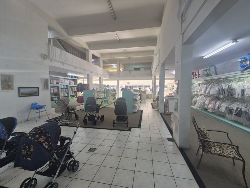 Spacious open-plan retail area featuring a mezzanine level, tiled and carpeted flooring, and structural columns, suitable for various commercial display purposes.