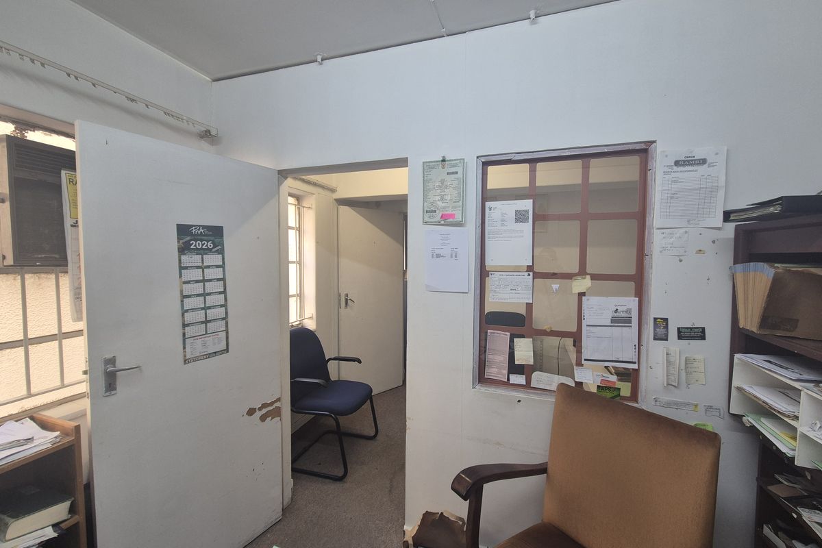 A functional office space featuring an internal service window, security bars on windows, and standard door access, requiring cosmetic updates to improve the interior finish.