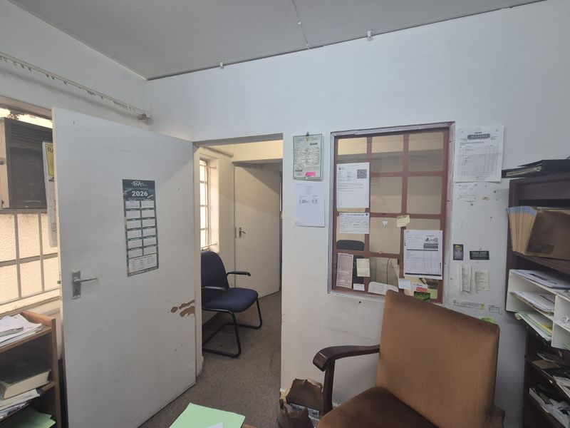 A functional office space featuring an internal service window, security bars on windows, and standard door access, requiring cosmetic updates to improve the interior finish.