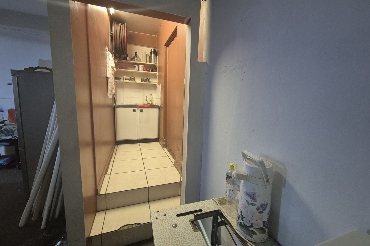 A small scullery or utility area featuring built-in cabinetry, tiled flooring, and a sink, accessible via a small step.