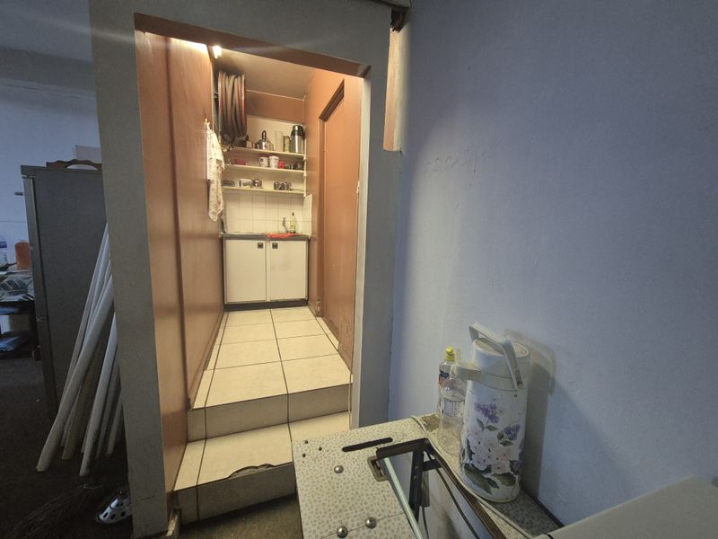 A small scullery or utility area featuring built-in cabinetry, tiled flooring, and a sink, accessible via a small step.