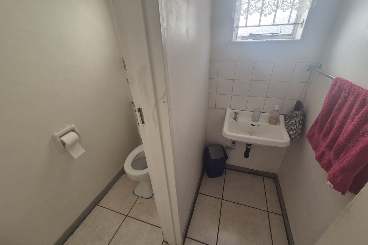 A compact bathroom featuring a wall-mounted basin, a separate toilet area, tiled flooring, and a window with security bars.