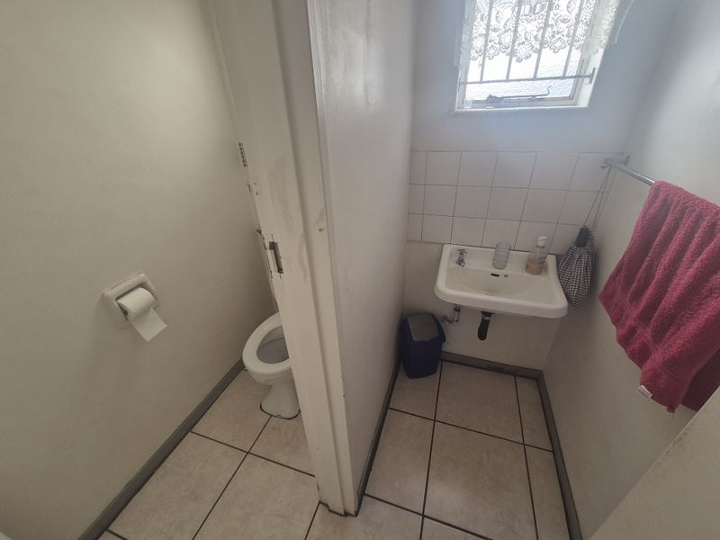 A compact bathroom featuring a wall-mounted basin, a separate toilet area, tiled flooring, and a window with security bars.
