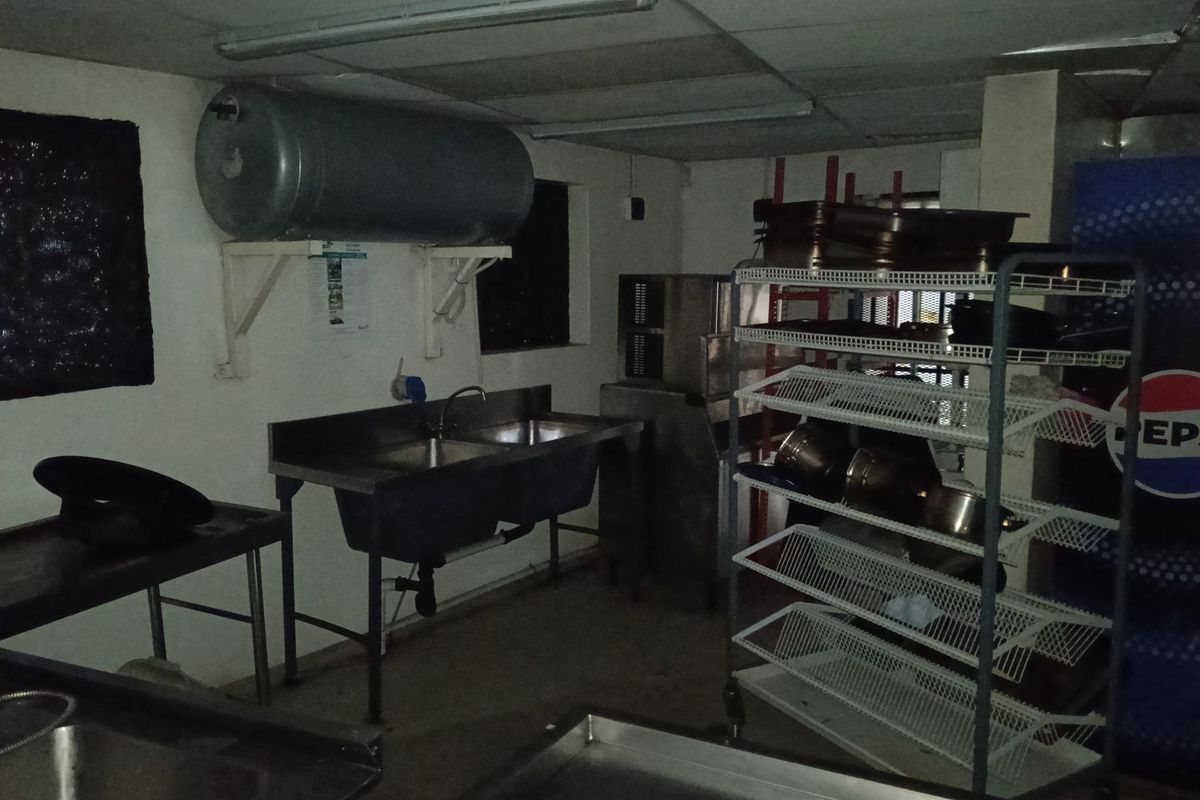 A functional commercial kitchen prep area featuring stainless steel double sinks, wall-mounted water heater, and industrial shelving units.