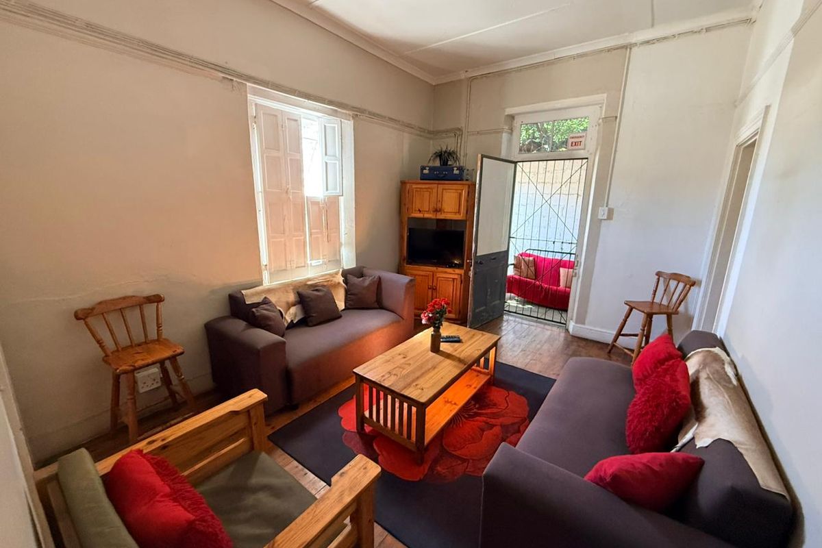 A living room featuring wooden flooring, a security gate at the entrance, and traditional window shutters.