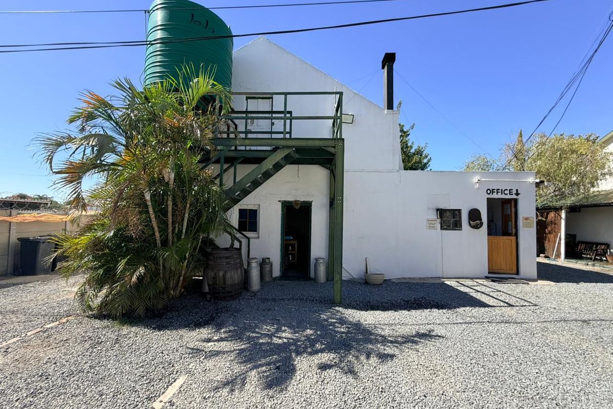 Exterior view of a guest house building featuring a prominent water tank, external metal staircase, and a designated office entrance.
