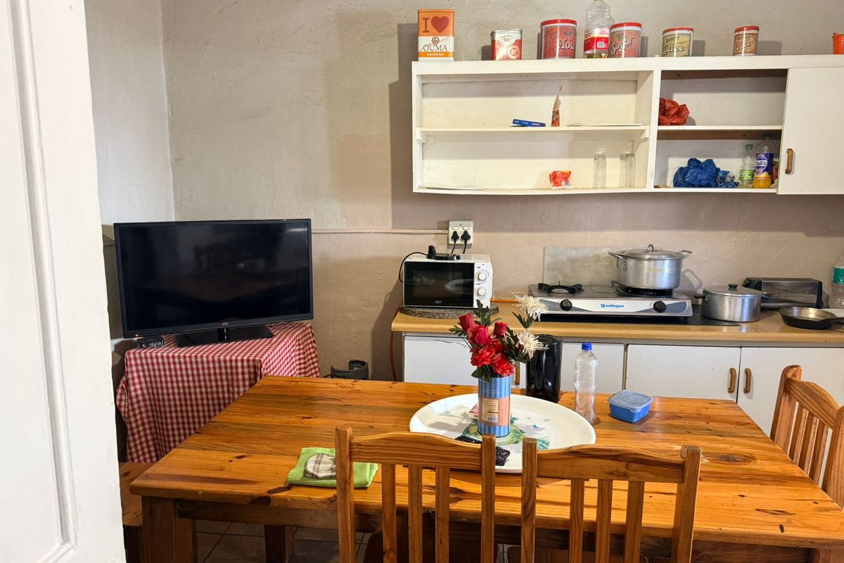 A compact kitchen and dining area featuring basic cabinetry, a gas hob, and tiled flooring, suitable for a functional guest house kitchenette.