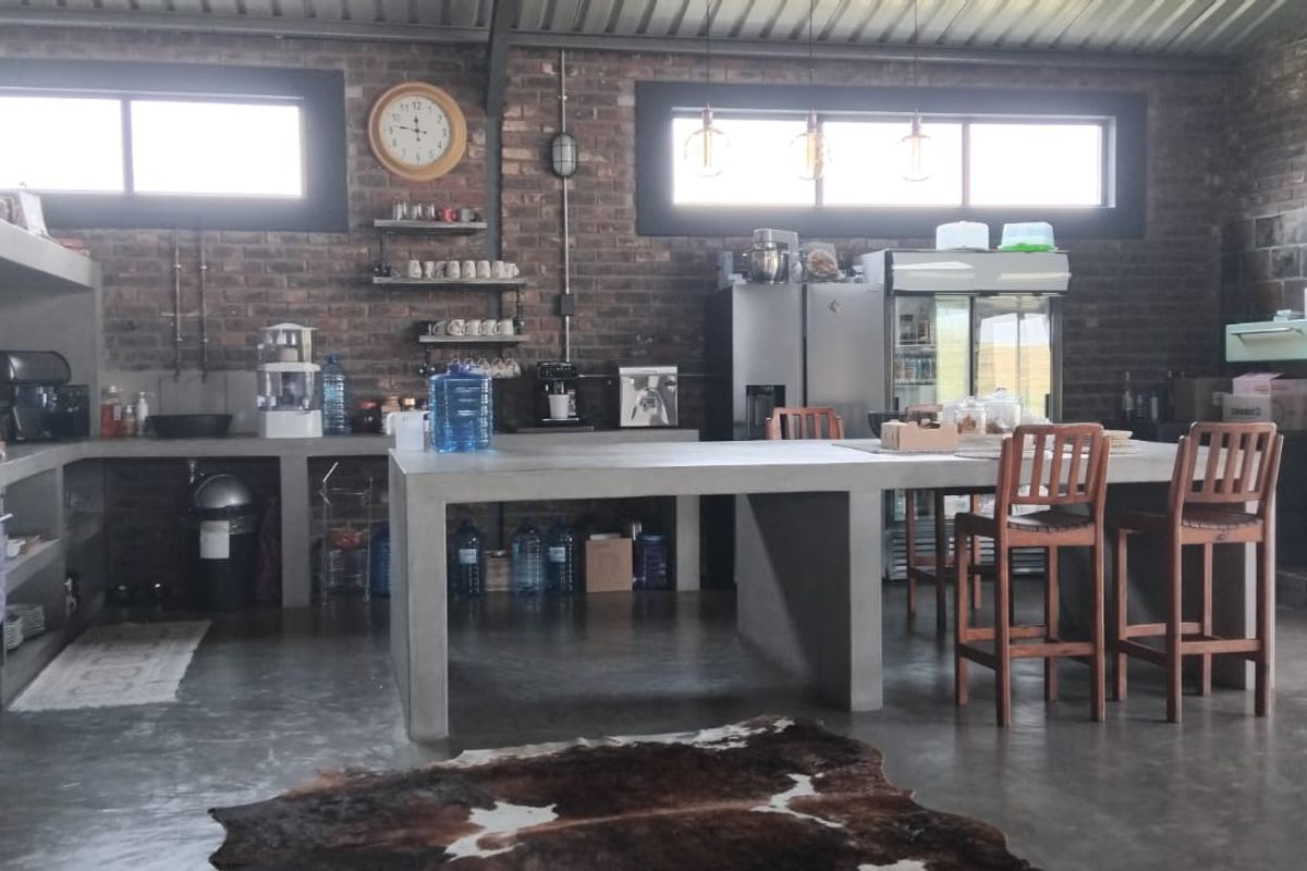 Spacious industrial-style kitchen featuring exposed brick walls, polished concrete floors, a large concrete island, and high-level windows providing ample natural light.