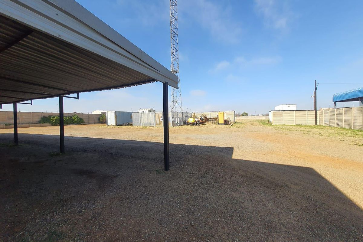 Expansive outdoor yard area featuring a covered parking structure, perimeter walling, and a tall communication mast on a gravel surface.