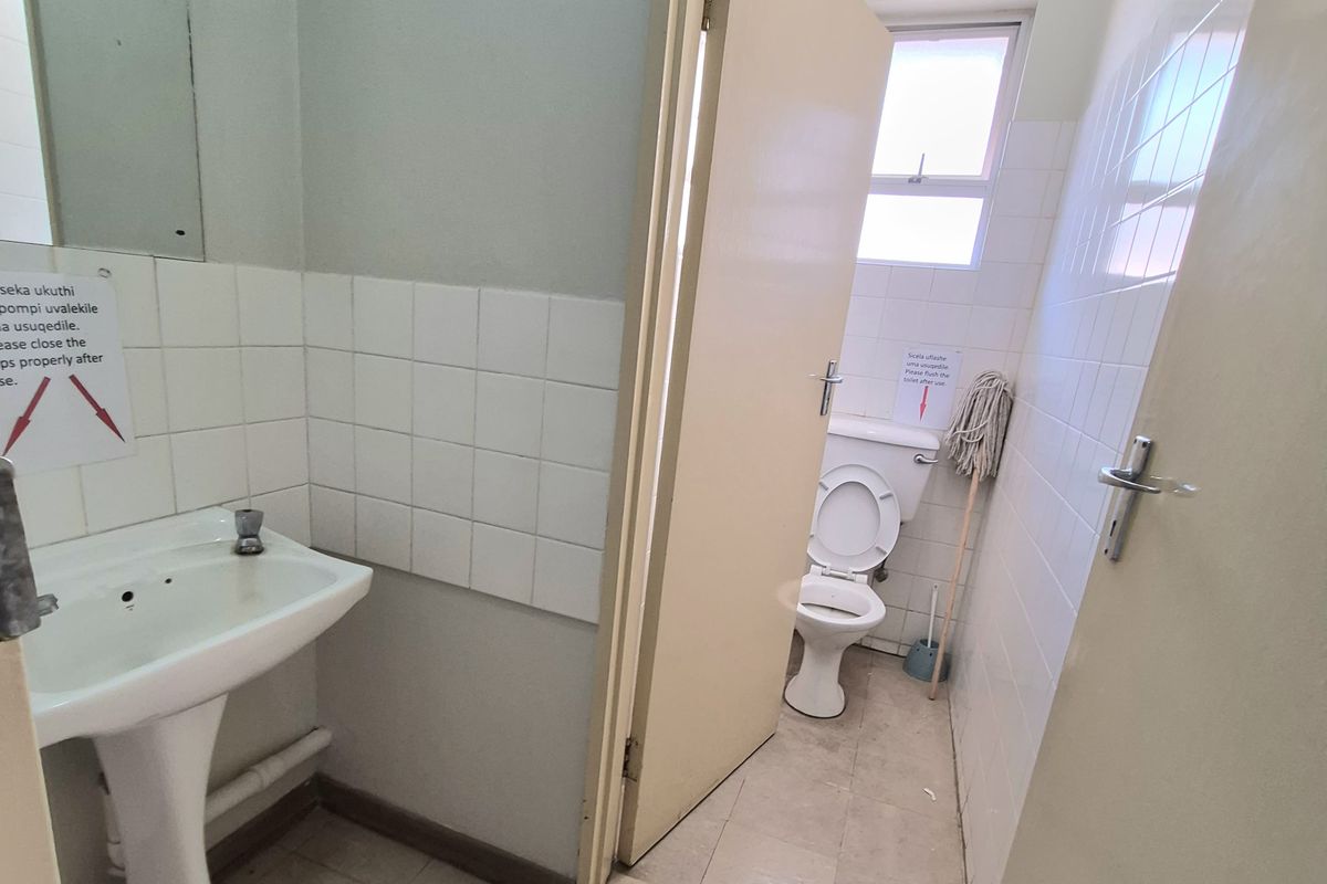 A functional office bathroom featuring a pedestal washbasin and a separate toilet cubicle with basic ceramic tiling and standard fixtures.