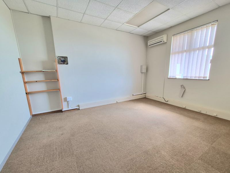 An empty office space featuring a suspended ceiling, split-system air conditioning, vertical blinds, and carpet flooring, ready for professional fit-out.