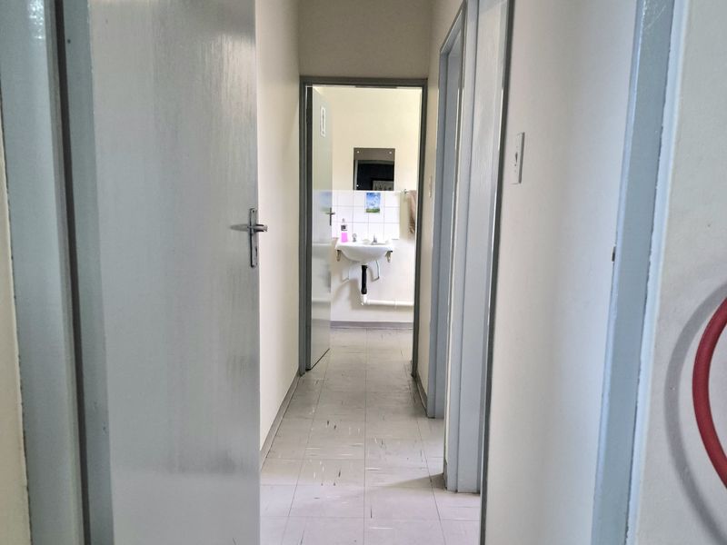 A functional office hallway featuring tiled flooring and leading to a small washroom area with a pedestal basin.