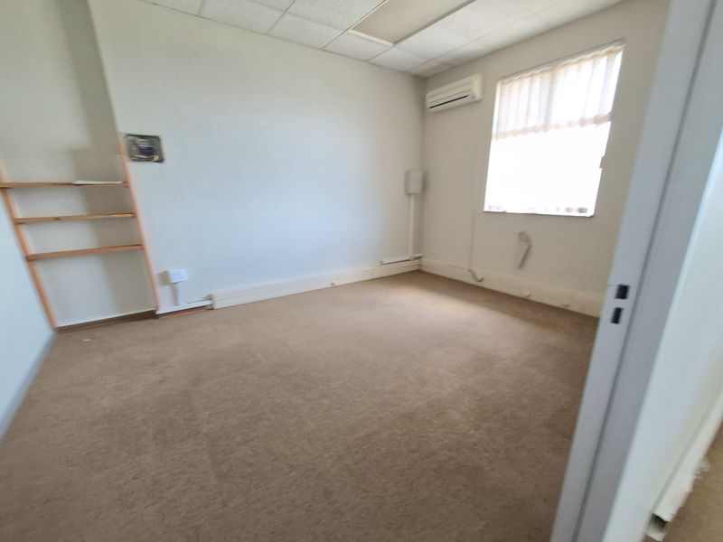A vacant office space featuring carpet flooring, a suspended ceiling, and a wall-mounted air conditioning unit, ready for customization.