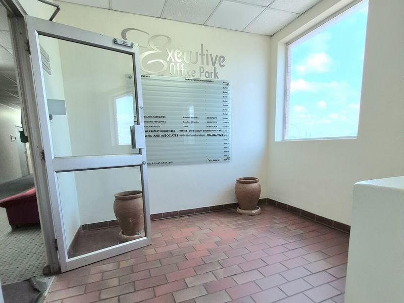 A bright office park entrance lobby featuring tiled flooring, a drop ceiling with track lighting, and a glass directory board.