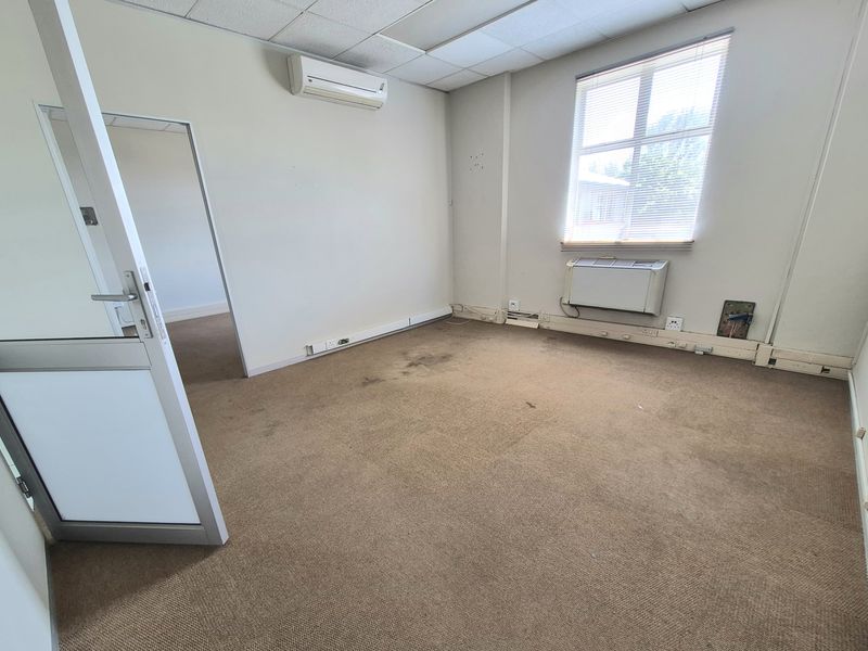 An empty office space featuring a suspended ceiling, split-system air conditioning, and wall-mounted heating unit, requiring carpet replacement and general cosmetic refurbishment.