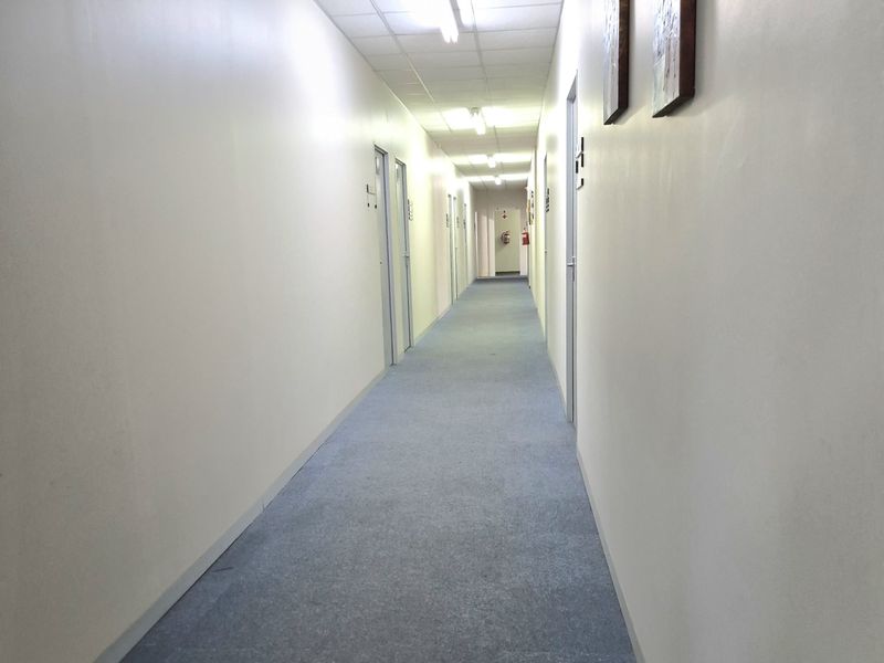 A long, functional office hallway featuring carpeted flooring, suspended ceiling tiles, and multiple access doors leading to individual office spaces.