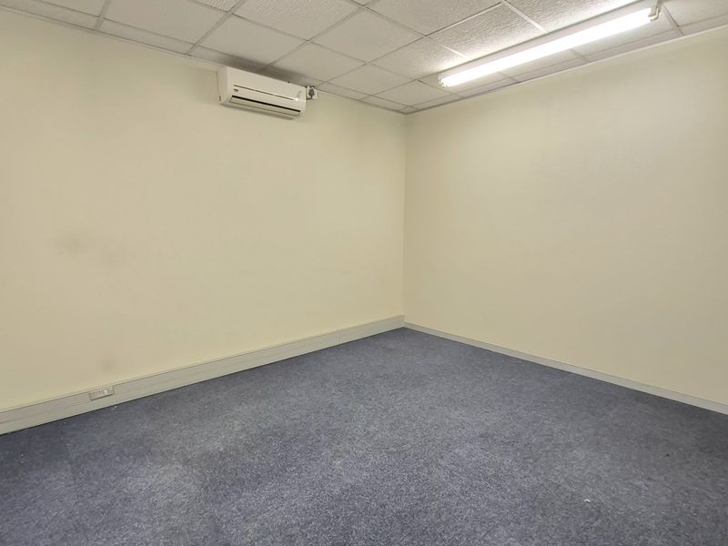 A clean, empty office space featuring a suspended ceiling, fluorescent lighting, split-system air conditioning, and carpeted flooring.
