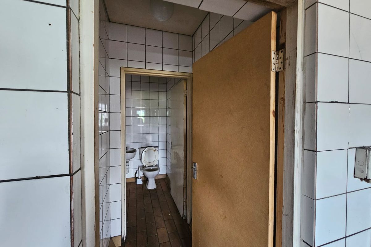 A small, dated bathroom featuring tiled walls and floors, equipped with a standard toilet and washbasin, requiring cosmetic updates and refurbishment.