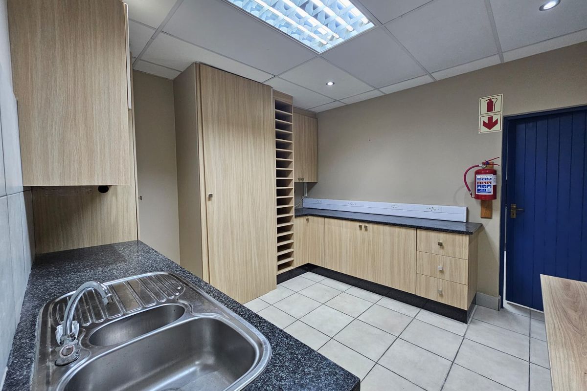 A clean, functional kitchen or utility area featuring light wood-grain cabinetry, granite countertops, a double sink, and professional drop-ceiling lighting.