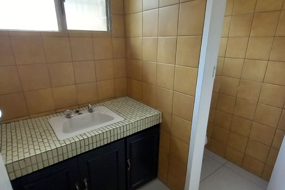 A functional office bathroom featuring a built-in vanity with a drop-in sink and full-height wall tiling.