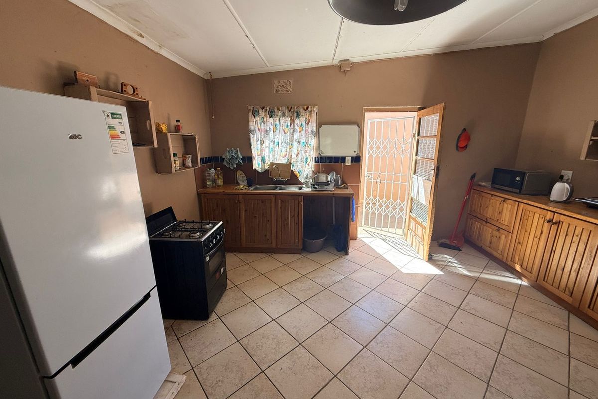 A functional kitchen featuring wooden cabinetry, tiled flooring, and direct access to the exterior through a security gate.