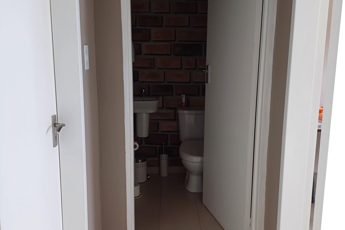A view from a hallway into a small bathroom featuring a toilet, pedestal basin, and exposed brick feature wall.