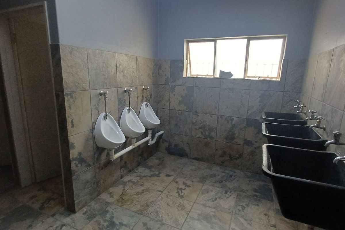 Industrial restroom facility featuring wall-mounted urinals and multiple utility sinks with tiled walls and flooring.