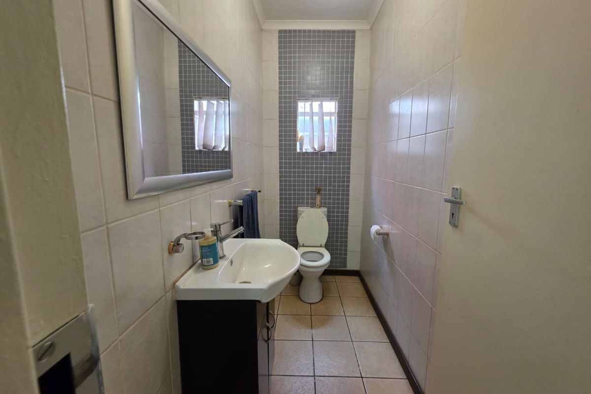 A functional bathroom featuring a wall-mounted vanity with basin, a toilet, and tiled walls with a decorative mosaic accent strip.